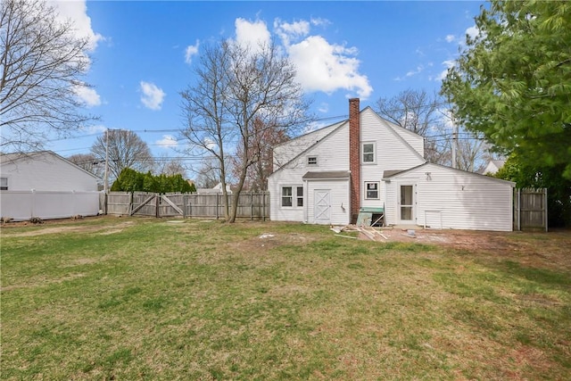 back of house featuring a yard, a fenced backyard, a gate, and a chimney