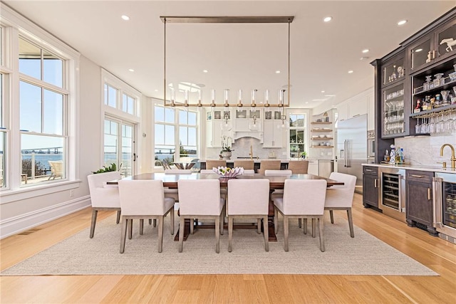 dining area featuring light wood-type flooring, beverage cooler, recessed lighting, and wet bar
