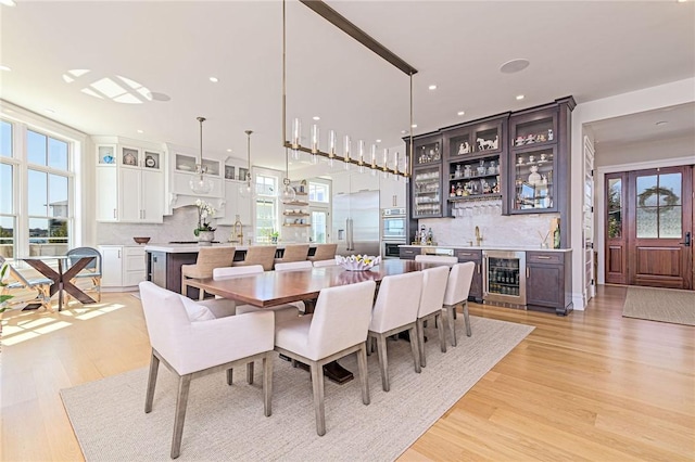dining space featuring beverage cooler, a healthy amount of sunlight, light wood finished floors, and bar