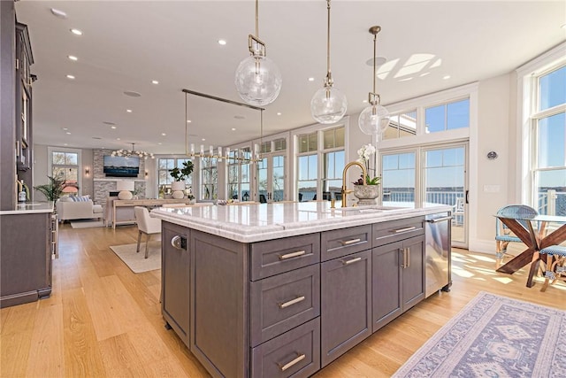 kitchen featuring light wood finished floors, stainless steel dishwasher, a sink, recessed lighting, and an island with sink