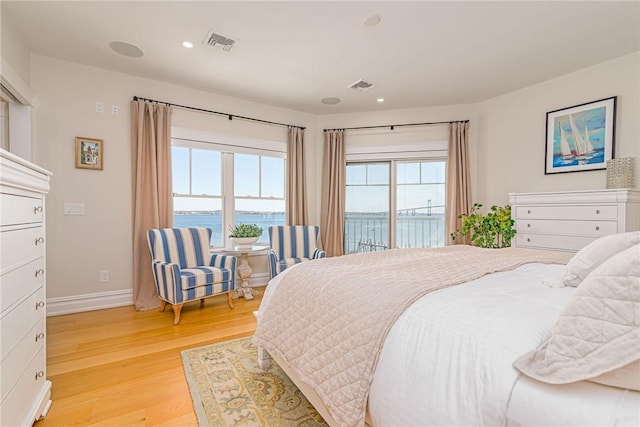 bedroom featuring light wood-style floors, visible vents, access to outside, and a water view
