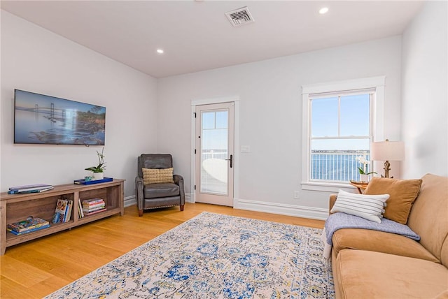 living area featuring light wood-type flooring, plenty of natural light, baseboards, and visible vents