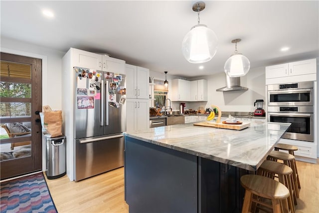 kitchen with a sink, wall chimney range hood, white cabinetry, and stainless steel appliances
