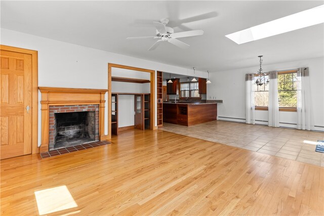 200 Pond St, South Kingstown, RI 02879 - unfurnished living room featuring light wood-style flooring, a skylight, ceiling fan with notable chandelier, and a fireplace