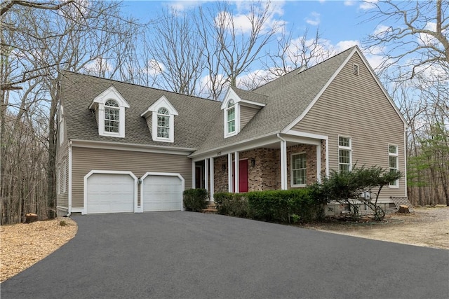 new england style home with an attached garage, a shingled roof, and aphalt driveway