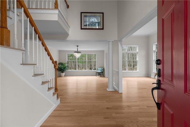 foyer entrance with crown molding, light wood-style floors, stairway, a high ceiling, and baseboards