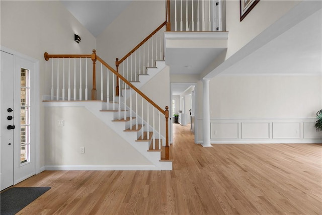 entrance foyer with a decorative wall, a towering ceiling, stairway, a wainscoted wall, and wood finished floors