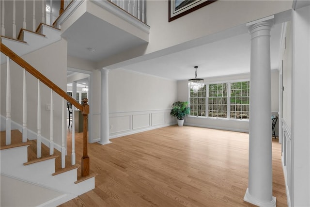 foyer featuring ornate columns, a decorative wall, stairs, and light wood-type flooring