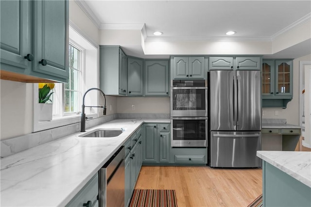 kitchen featuring crown molding, light wood-type flooring, light stone counters, a sink, and stainless steel appliances