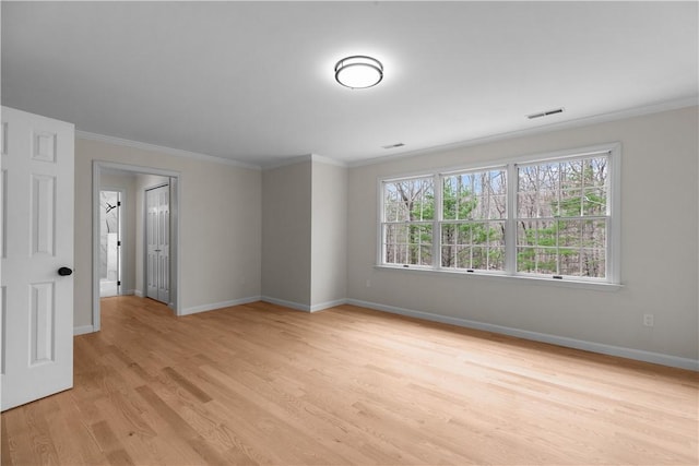 spare room with light wood finished floors, visible vents, baseboards, and ornamental molding