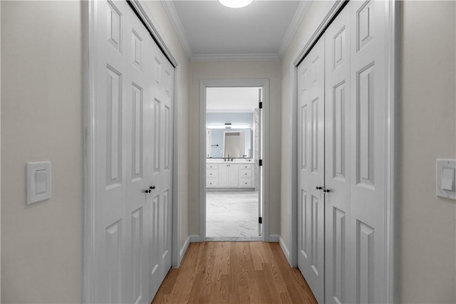 hallway with light wood-style flooring, baseboards, and crown molding