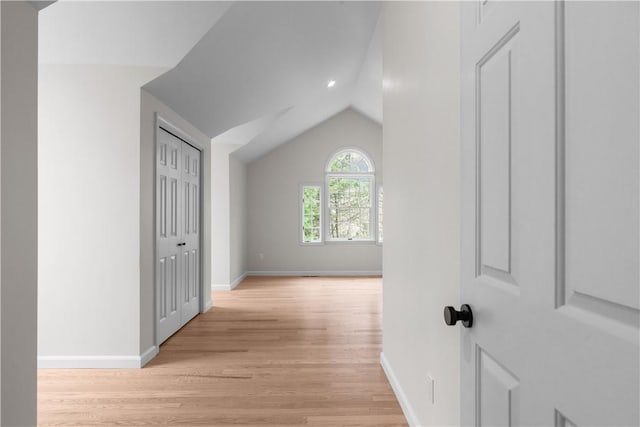 corridor featuring light wood-style floors, baseboards, and vaulted ceiling