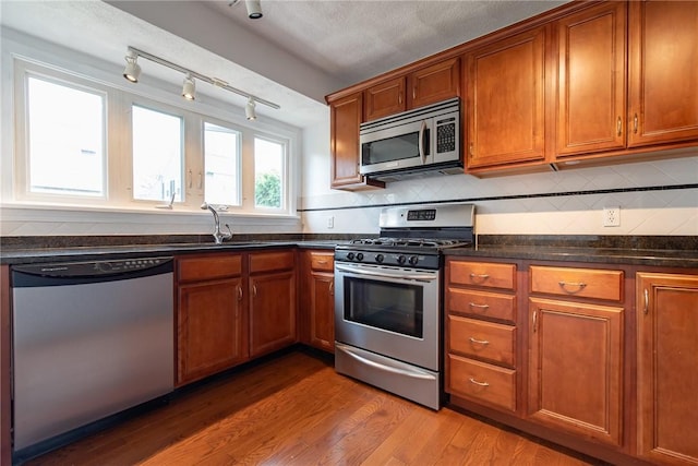 83 Wyndham Ave, Providence, RI 02908 - kitchen with a sink, appliances with stainless steel finishes, brown cabinetry, backsplash, and light wood-style flooring