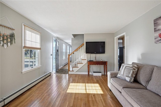living area featuring hardwood / wood-style floors, a baseboard heating unit, baseboards, and stairs