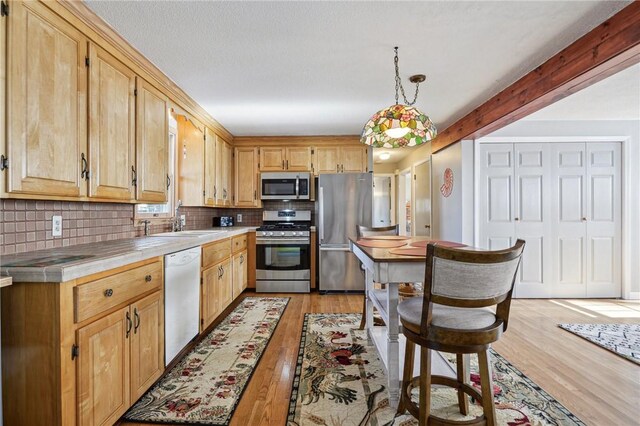 kitchen featuring tile countertops, light wood-type flooring, a sink, stainless steel appliances, and backsplash