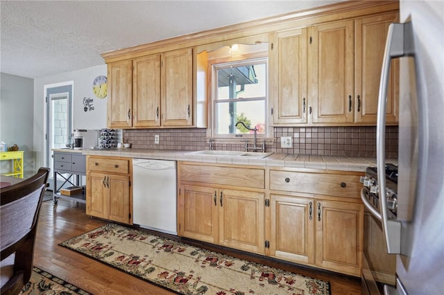 kitchen with a sink, appliances with stainless steel finishes, dark wood finished floors, tile counters, and backsplash