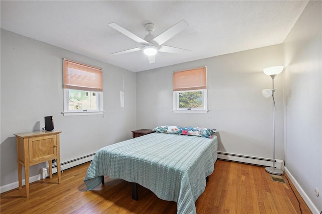 bedroom with wood finished floors, a baseboard heating unit, and multiple windows