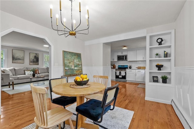 dining room featuring an inviting chandelier, a wealth of natural light, light wood-style flooring, arched walkways, and a baseboard heating unit