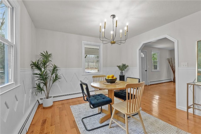 dining room featuring arched walkways, a baseboard heating unit, an inviting chandelier, and a wainscoted wall
