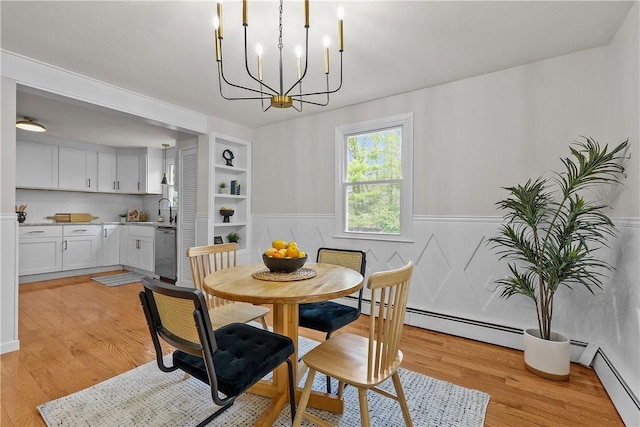 dining area featuring light wood-style flooring, a chandelier, a baseboard heating unit, wainscoting, and built in shelves