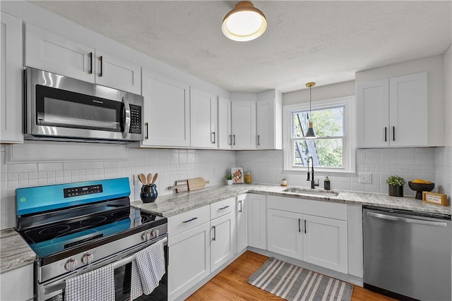 kitchen with a sink, white cabinets, appliances with stainless steel finishes, and light wood finished floors