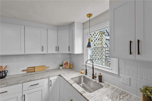 kitchen featuring white cabinets, tasteful backsplash, a sink, and light stone counters