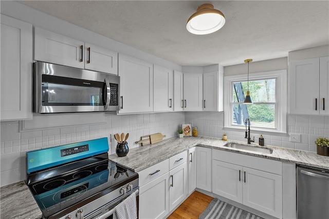 kitchen featuring a sink, white cabinetry, light stone countertops, backsplash, and stainless steel appliances