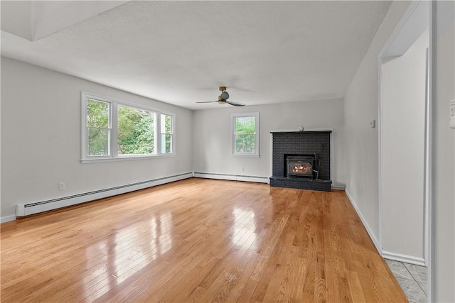 unfurnished living room featuring baseboard heating, ceiling fan, a fireplace, and light wood finished floors