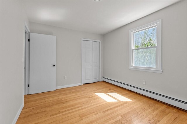 unfurnished bedroom with baseboard heating, light wood-type flooring, a closet, and baseboards