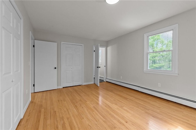 unfurnished bedroom with baseboard heating, light wood-type flooring, and baseboards