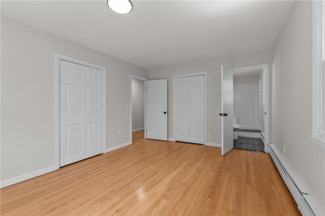 unfurnished bedroom with baseboard heating, baseboards, light wood-style flooring, two closets, and connected bathroom