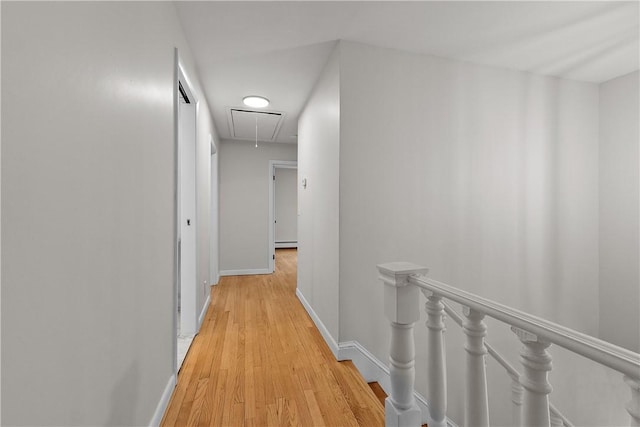 hall with an upstairs landing, light wood-style flooring, baseboards, and attic access