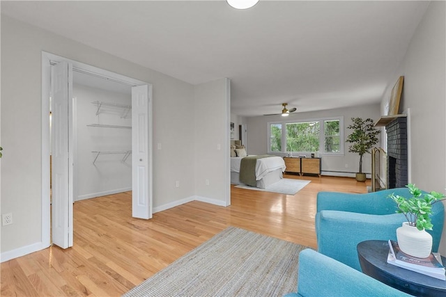 living area featuring baseboards, a fireplace, a ceiling fan, light wood-style floors, and a baseboard radiator