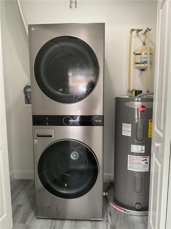 clothes washing area featuring wood finished floors, water heater, stacked washer / drying machine, baseboards, and laundry area
