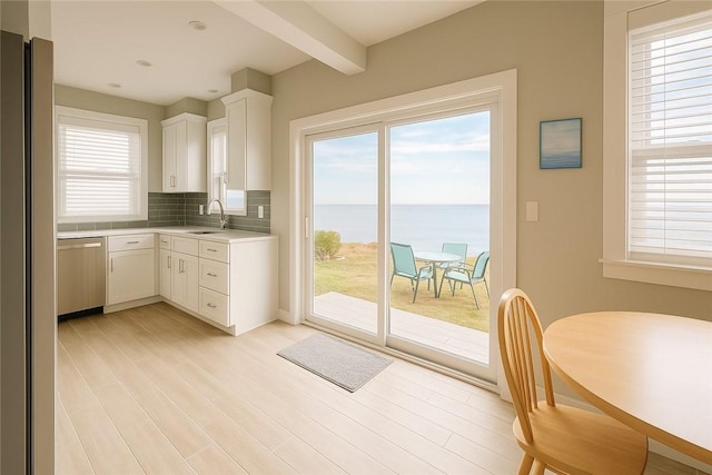 kitchen featuring tasteful backsplash, white cabinets, appliances with stainless steel finishes, light countertops, and a sink