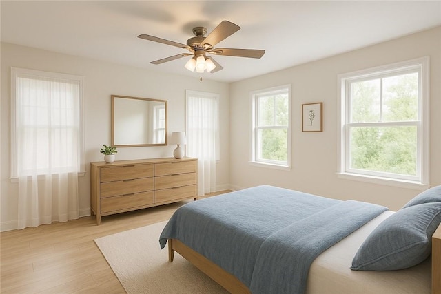 bedroom featuring a ceiling fan, baseboards, multiple windows, and light wood finished floors