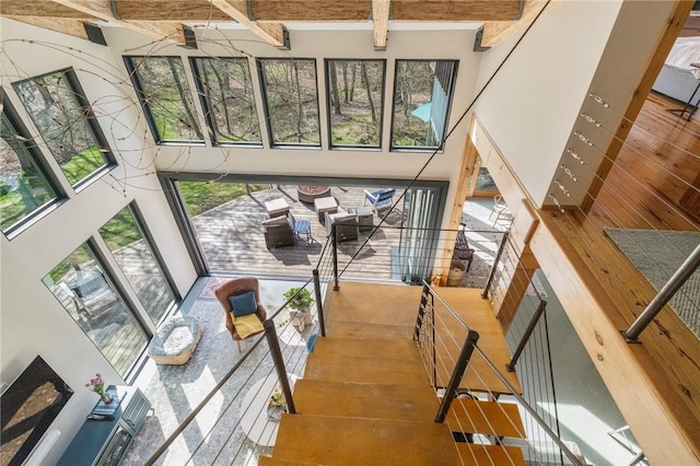 stairs featuring beam ceiling, a towering ceiling, and wood finished floors