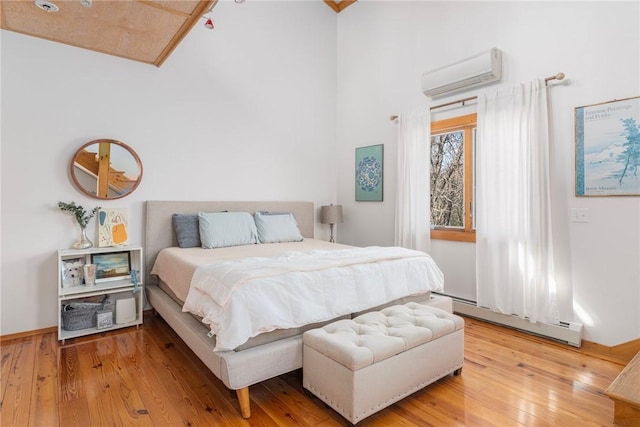 bedroom with a wall mounted air conditioner, a high ceiling, light wood-style flooring, and a baseboard radiator
