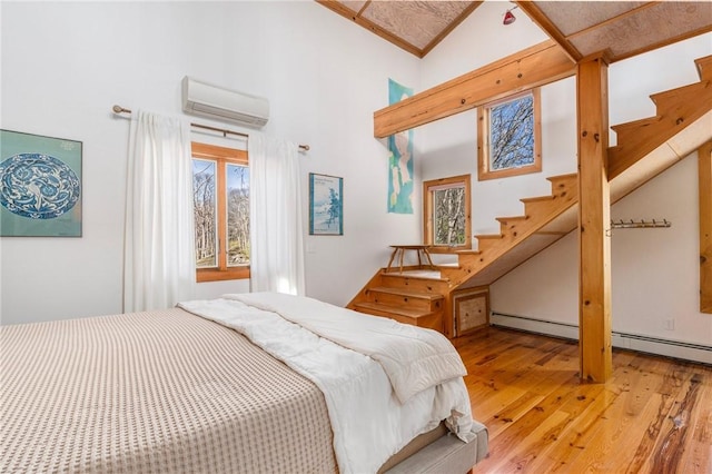 bedroom with baseboard heating, a wall mounted air conditioner, light wood-style floors, and a high ceiling
