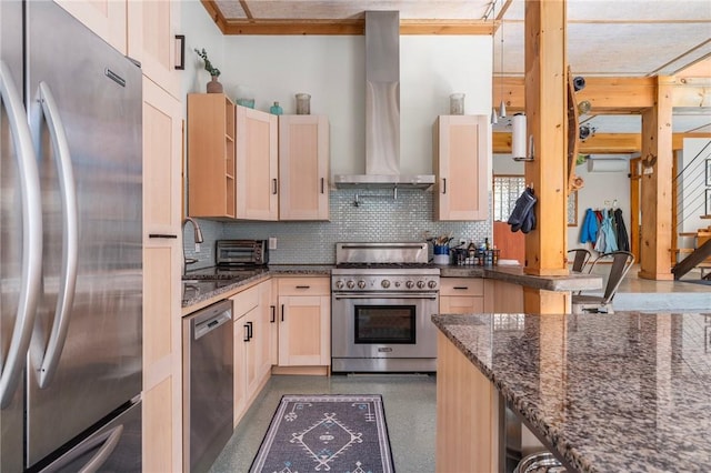 kitchen featuring dark stone countertops, tasteful backsplash, light brown cabinets, stainless steel appliances, and wall chimney exhaust hood