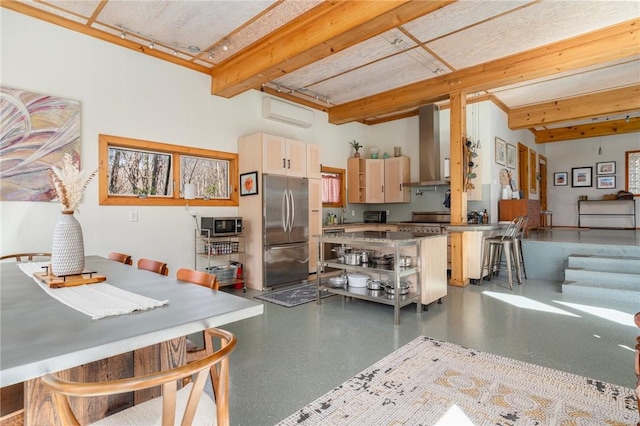 kitchen with beam ceiling, stainless steel appliances, speckled floor, and wall chimney range hood