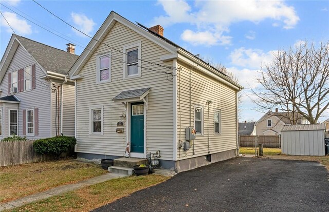 77 Seamans St, Providence, RI 02908 - view of front of house with an outdoor structure, fence, a storage unit, and a chimney
