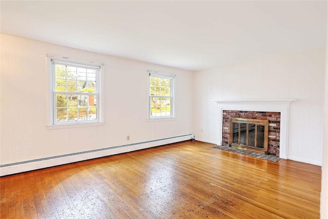 unfurnished living room with a baseboard radiator, a healthy amount of sunlight, wood-type flooring, and a brick fireplace