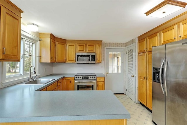 kitchen with light floors, a peninsula, appliances with stainless steel finishes, light countertops, and a sink