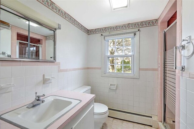 bathroom featuring a baseboard heating unit, a stall shower, toilet, wainscoting, and tile walls