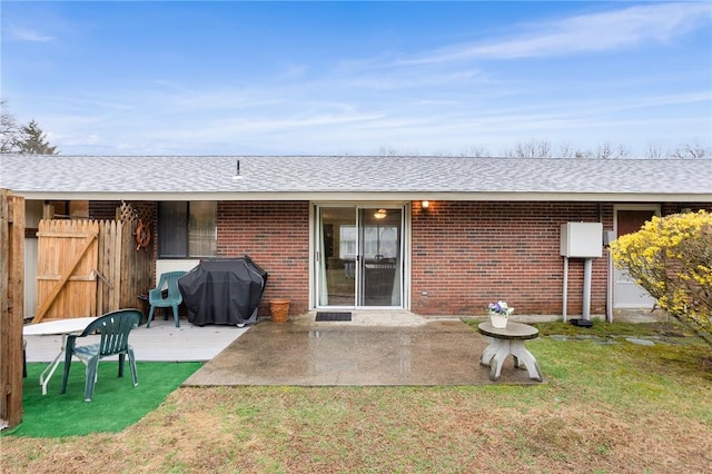 rear view of house featuring a shingled roof, brick siding, and a patio area