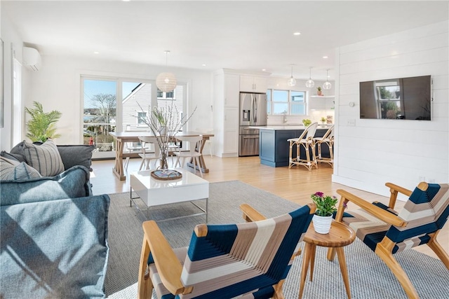 living room featuring recessed lighting, plenty of natural light, a wall unit AC, and light wood-style flooring