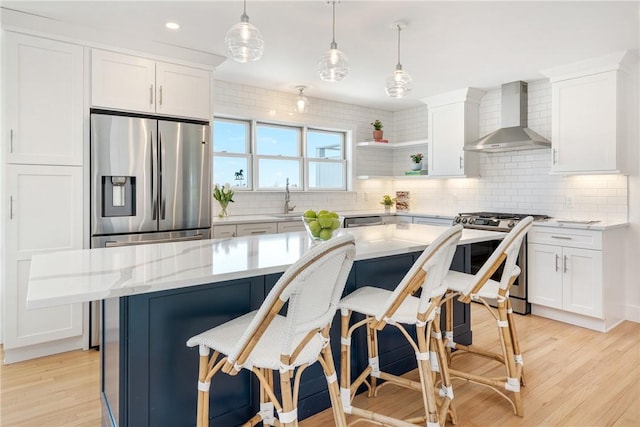 kitchen featuring stainless steel appliances, light wood-style floors, white cabinetry, decorative backsplash, and wall chimney range hood