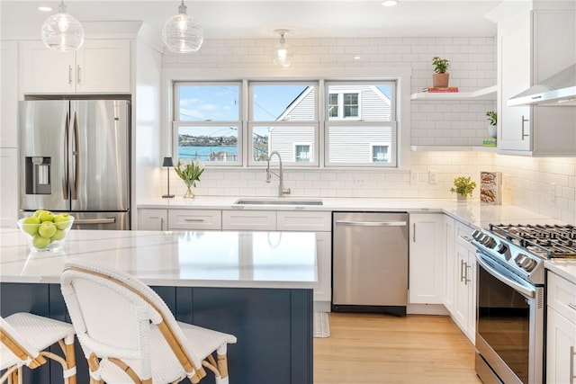 kitchen featuring wall chimney range hood, a sink, a breakfast bar, stainless steel appliances, and white cabinets