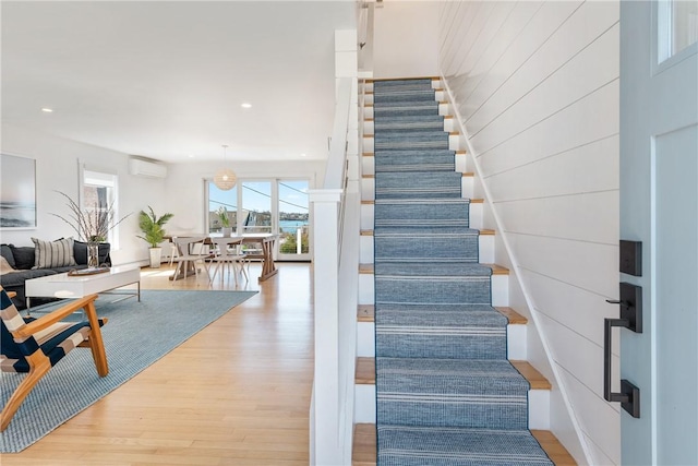 stairway with recessed lighting, wood finished floors, and a wall mounted air conditioner
